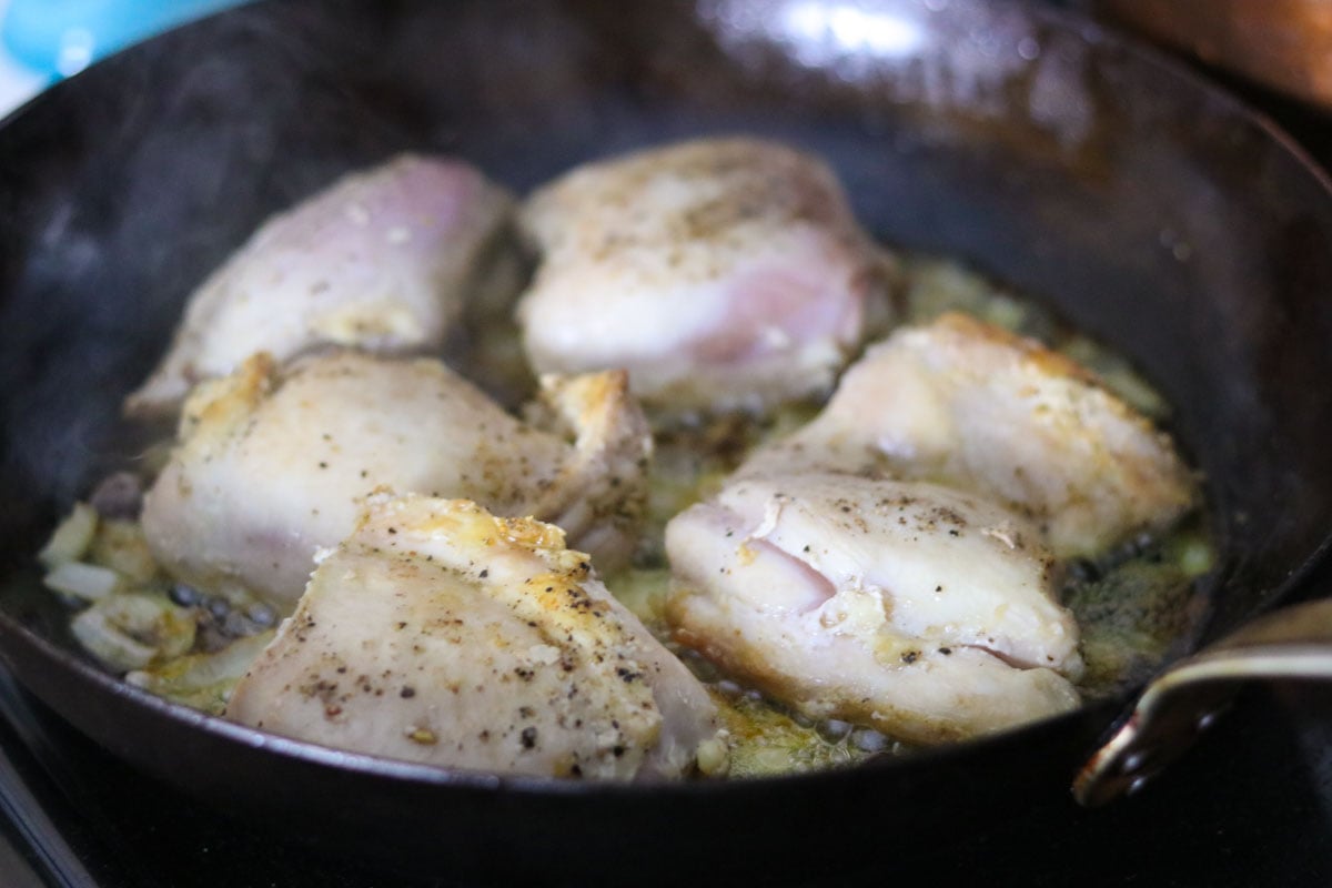 chicken thighs cooking over mushroom and onion in a carbon steel pan