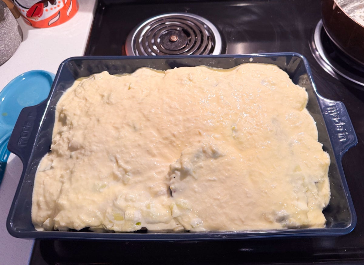 egg and yogurt mixture over musaka ingredients in a rectangular baking dish