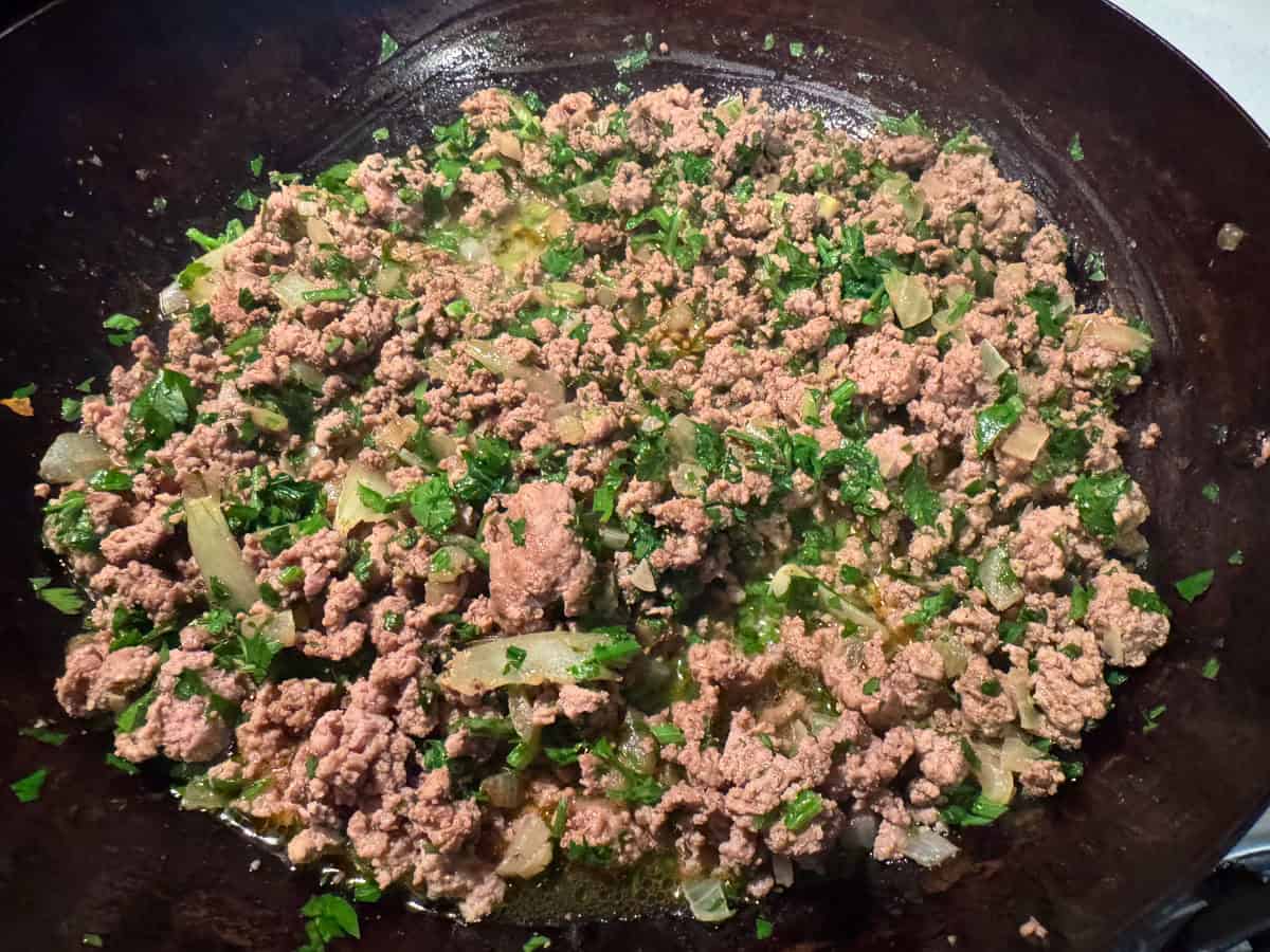 ground beef and chopped parsley cooking in a blue carbon steel pan