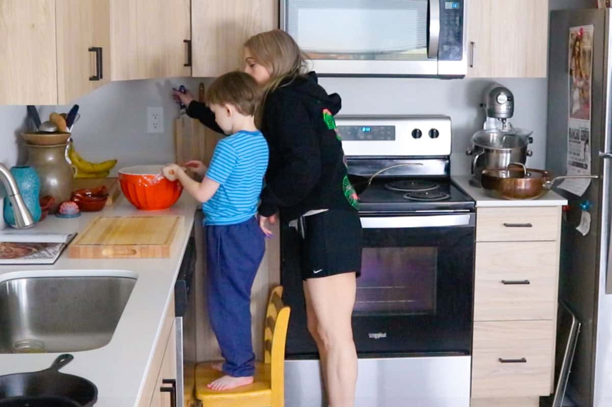 John is removing plastic wrap from a bowl and Kristin is grabbing a knife