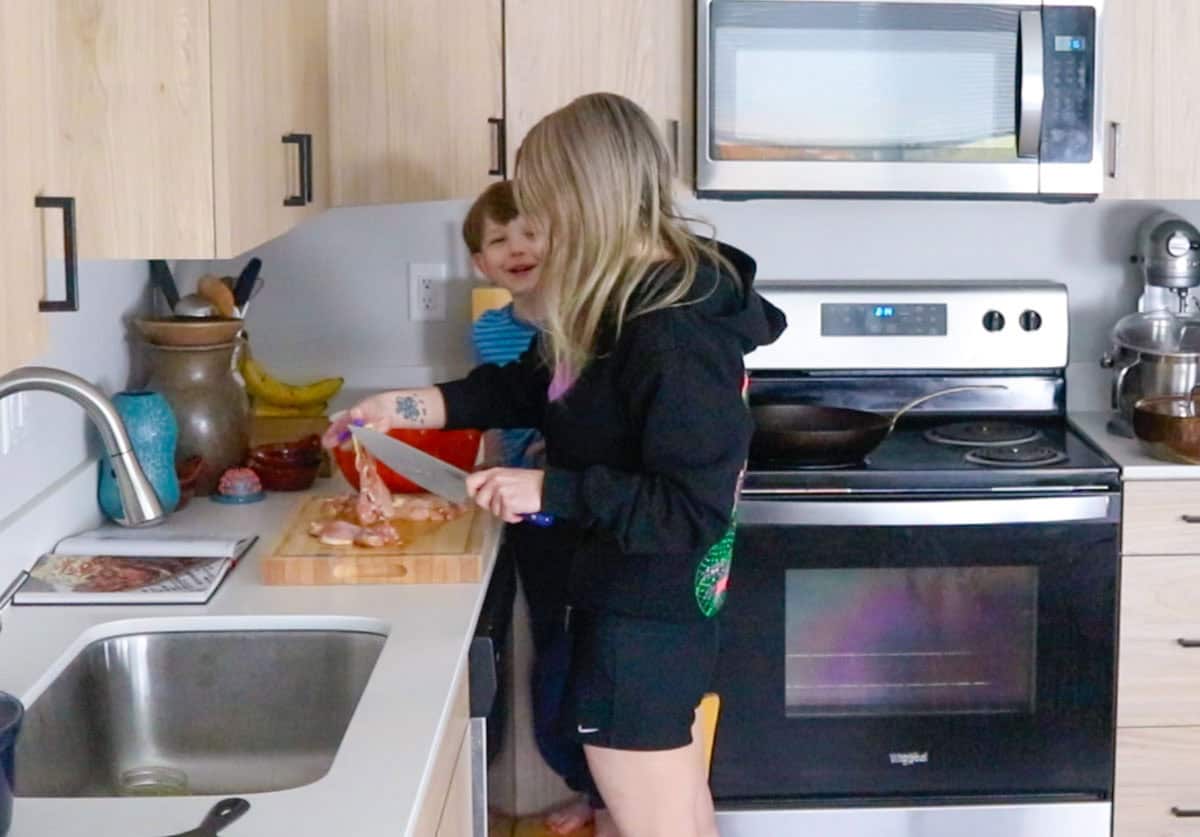 Kristin is cutting chicken thighs and talking to John