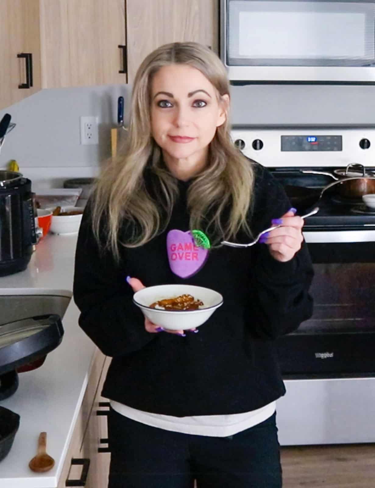 Kristin is holding a bowl of Korean chicken teriyaki and a fork, ready to dig in.