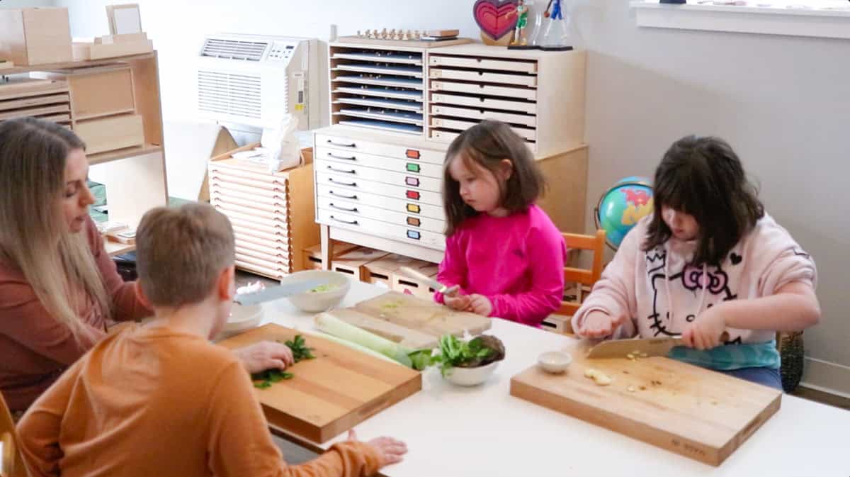 Kristin and the kids are prepping eggplant, onion, and parsley with a knife and a butcher block