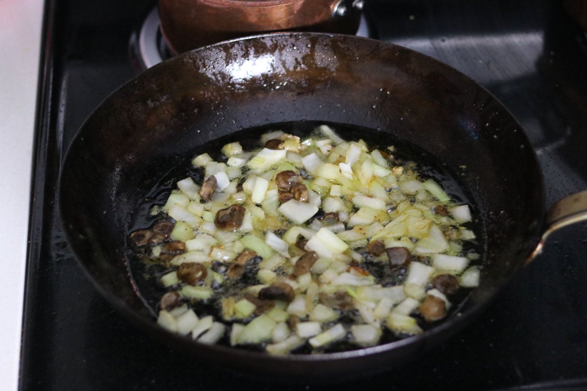 mushroom and onion cooking in a carbon steel pan