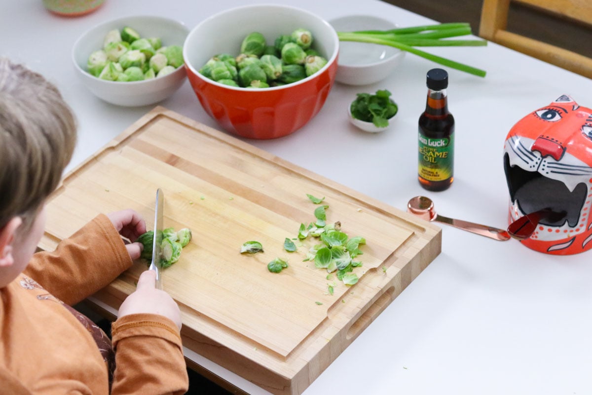 Noah is cutting Brussels sprouts in half with a Santoku knife