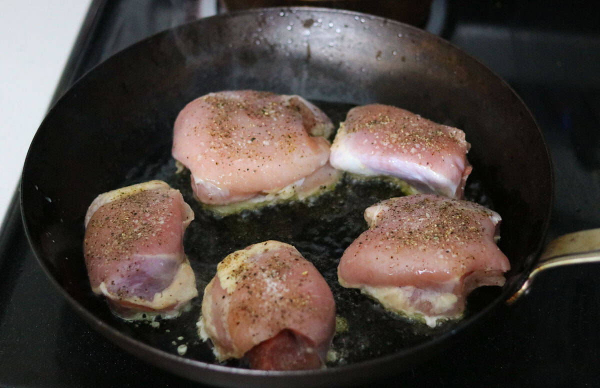 raw chicken thighs cooking in a carbon steel pan