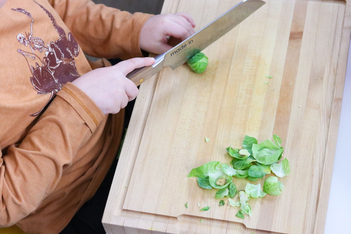 Noah is cutting Brussels sprouts in half with a Santoku knife