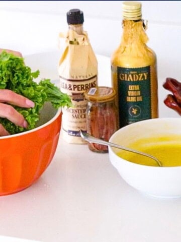 Caesar dressing in a bowl beside giadzy olive oil, worcestershire sauce, anchovies, and Kristin massaging some very lucky kale