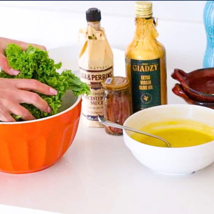 Caesar dressing in a bowl beside giadzy olive oil, worcestershire sauce, anchovies, and Kristin massaging some very lucky kale