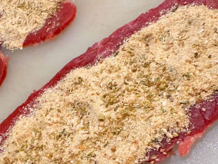 beef for braciole with breadcrumbs and spices on a cutting board