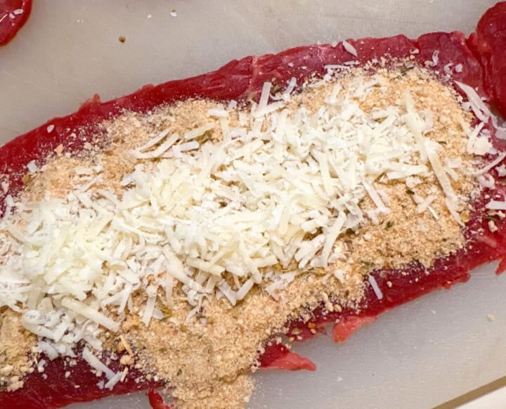 beef for braciole with breadcrumbs, spices, and parmesan cheese on a cutting board