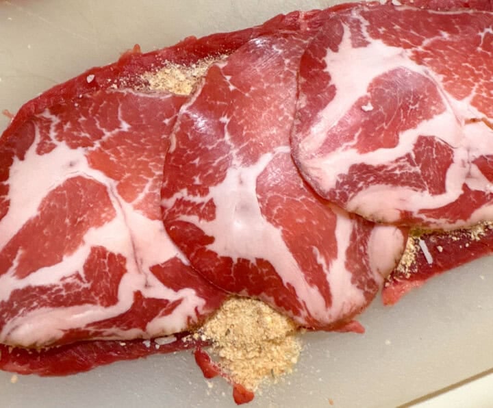 beef for braciole layered with breadcrumbs, spices, parmesan, and capicola on a cutting board