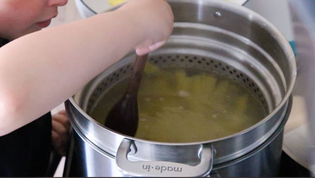 Noah is pushing the pasta down into the stock pot