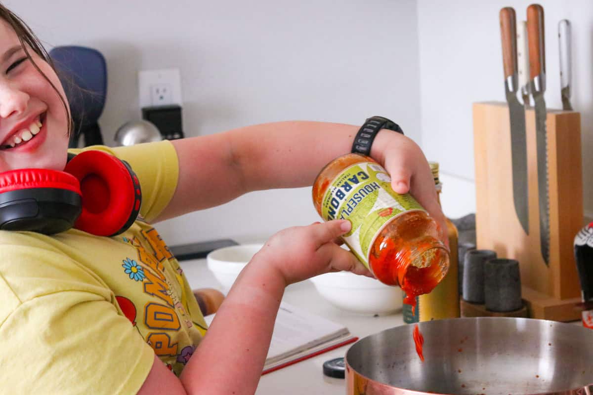 Kaia is laughing and adding marinara to a copper saucier