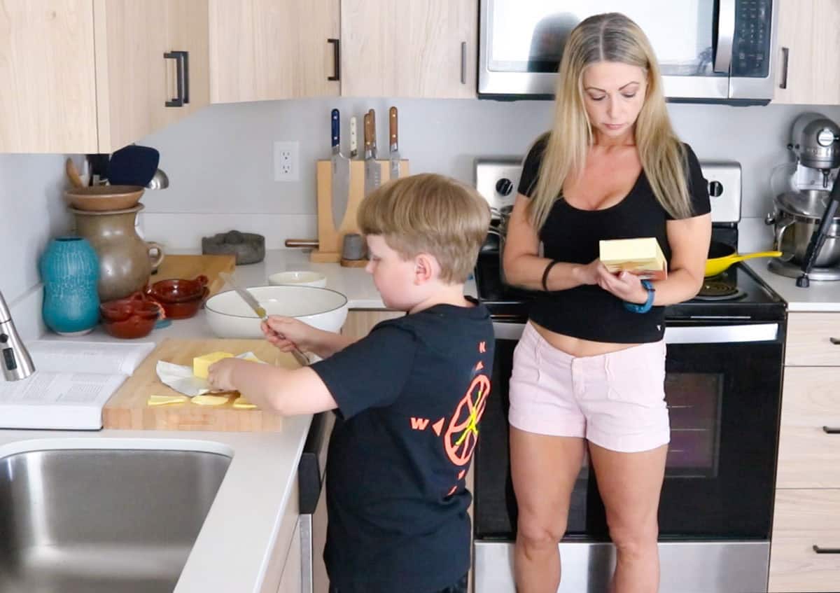 Noah is slicing a lot of butter and Kristin is reading the Giadzy pasta box