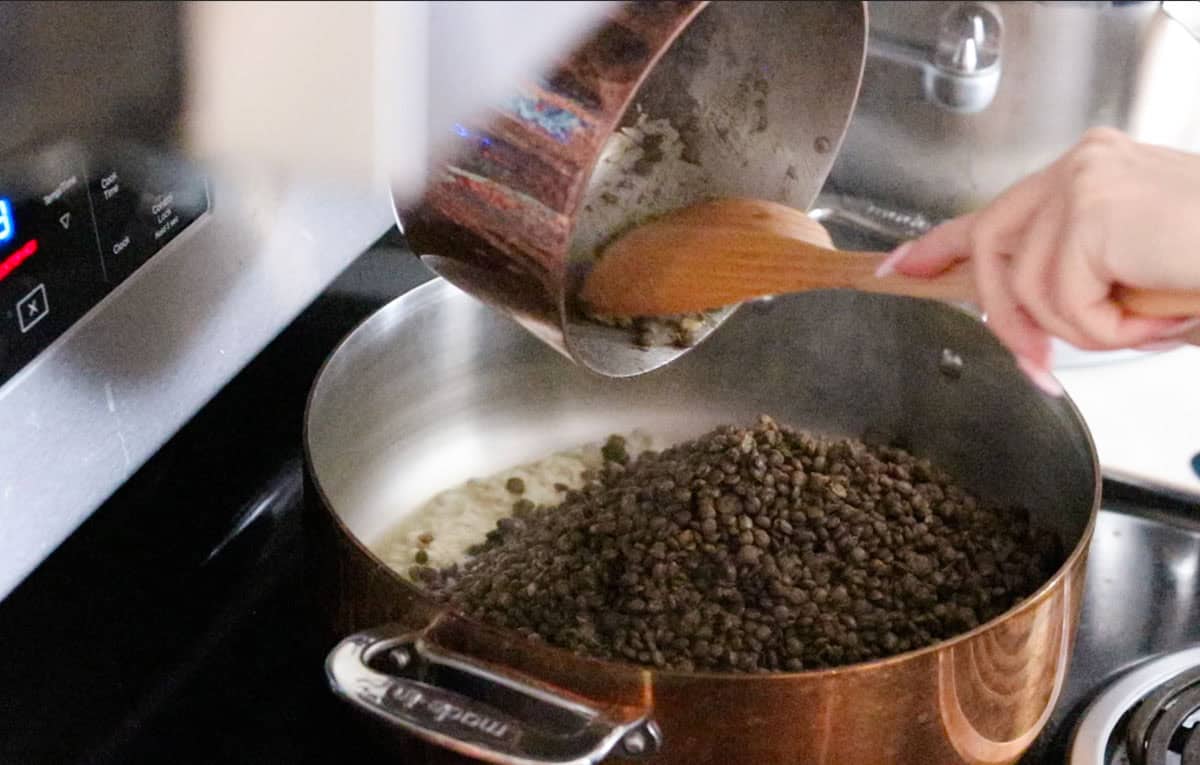 Kristin is transferring lentils to a rondeau with cooked rice and broth