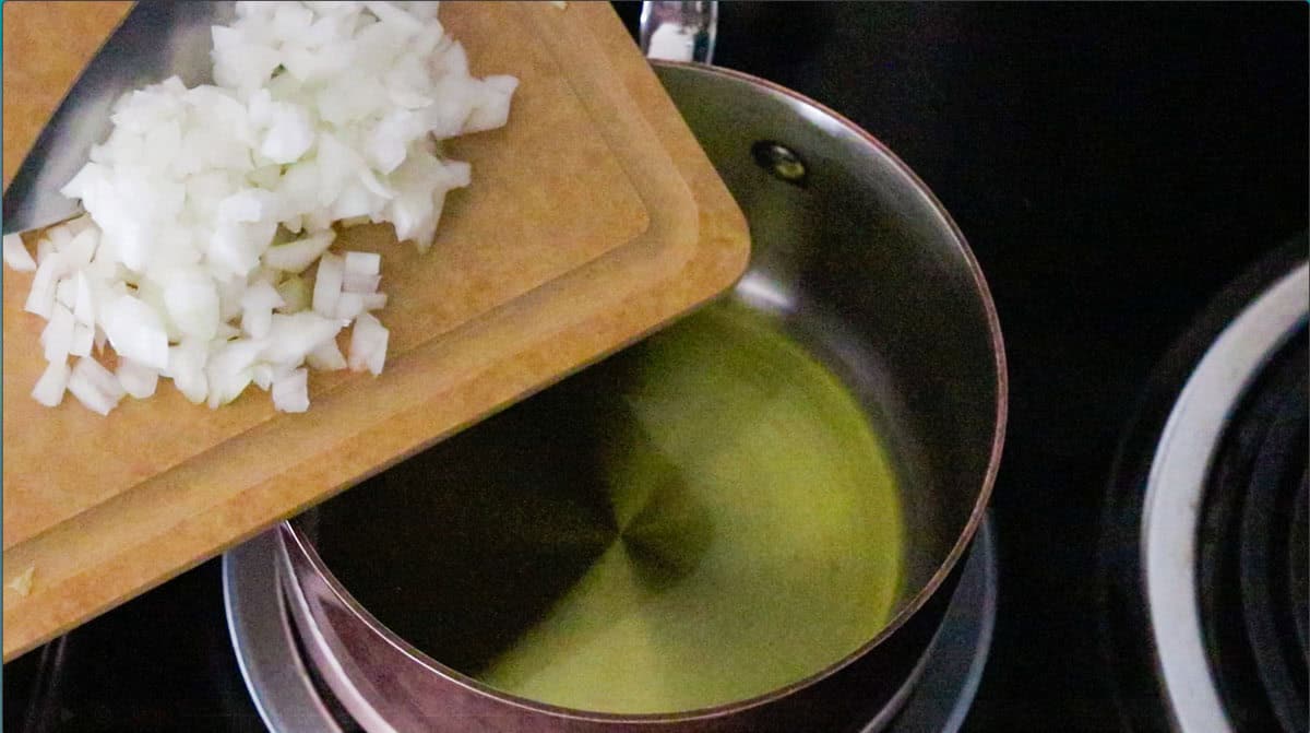 chopped onion on a cutting board over a saucepan with hot olive oil