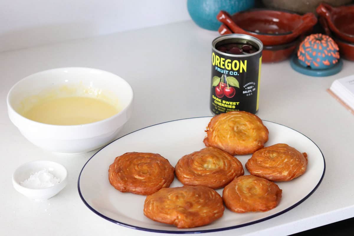 plate of zeppole beside, a bowl of custard, and a can of dark, sweet cheeries