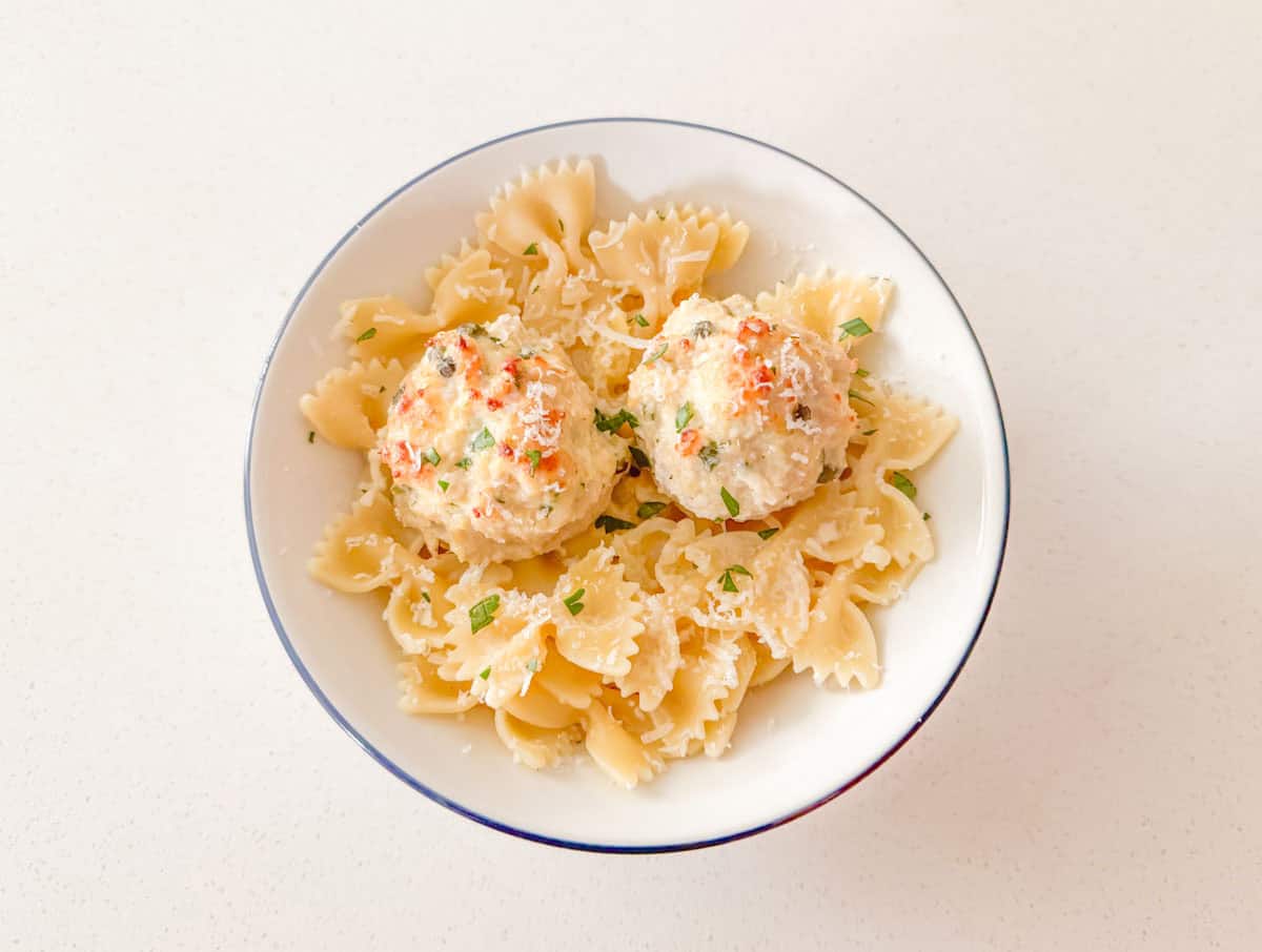 chicken piccata meatballs over a bowl of bowtie pasta