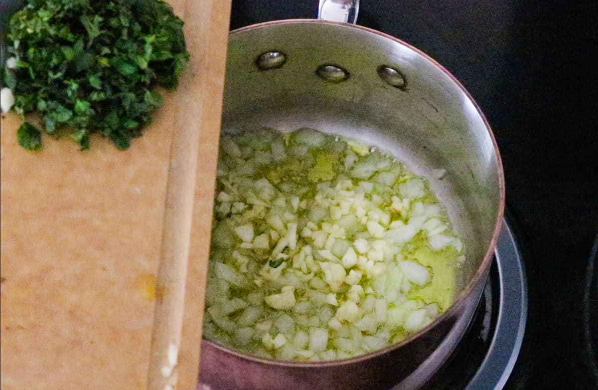 chopped oregano over a saucepan with chopped onion and garlic in oil