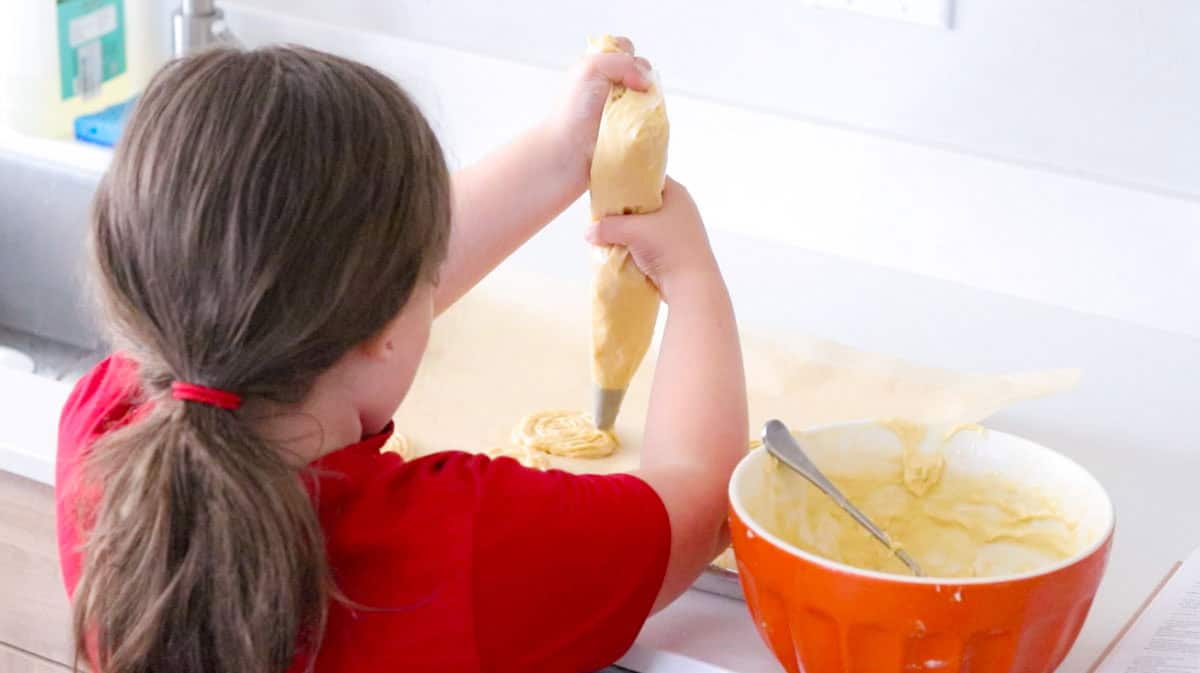 Kat is piping zeppole onto a lined baking sheet