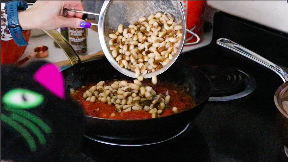 Kristin is adding cooked beans to a pan