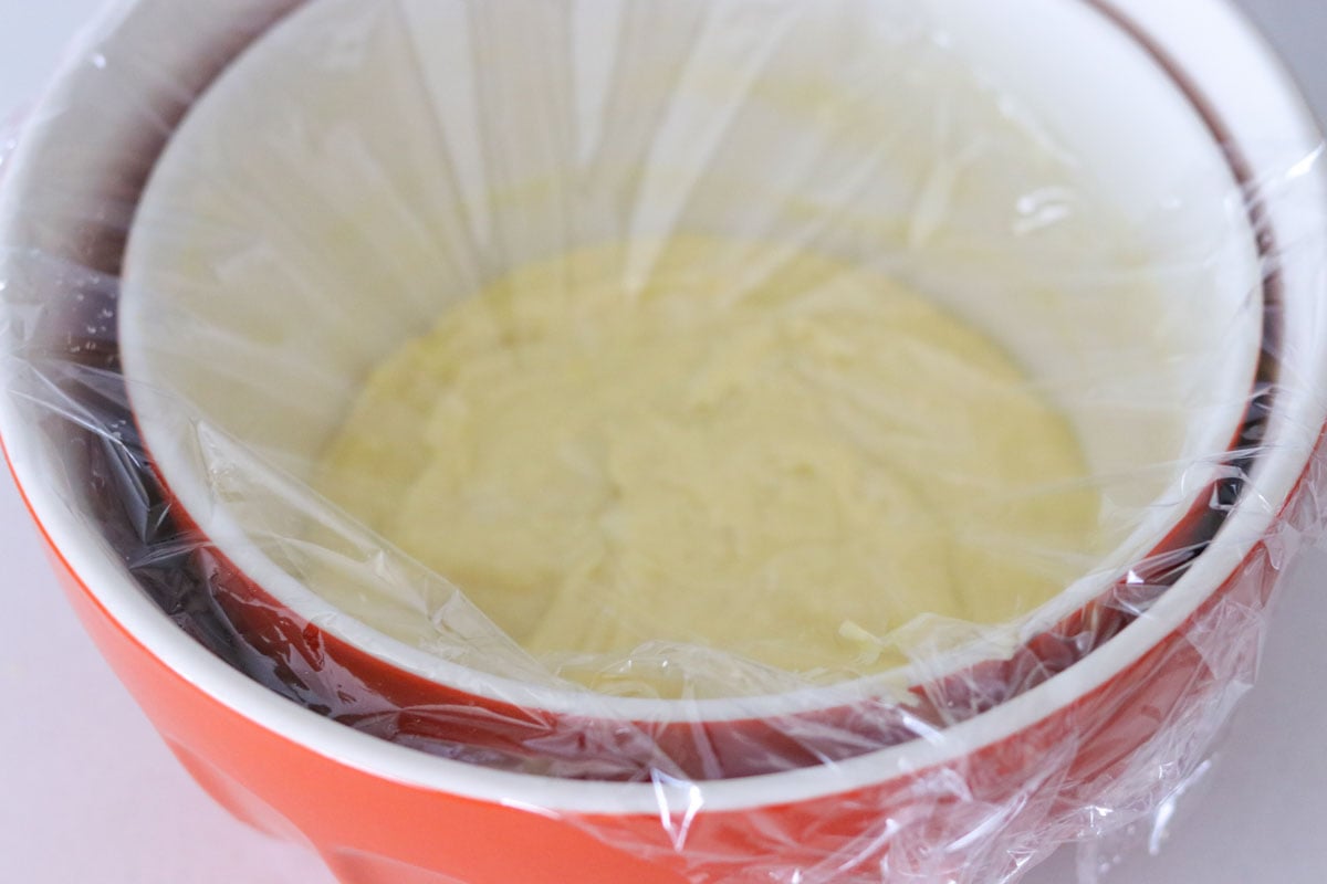 cooling custard in a bowl of ice water with the custard bowl placed inside. The custard bowl is covered with plastic wrap.