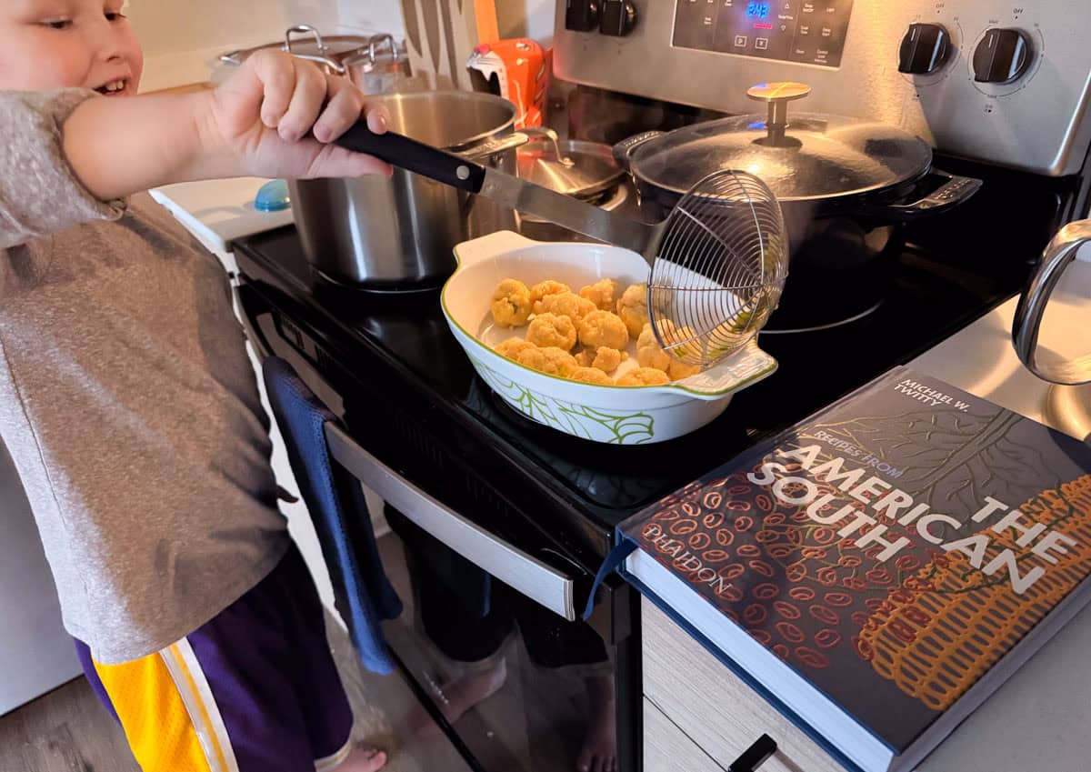 Noah is transferring corn dumplings from a stock pot to a serving dish using a spider strainer