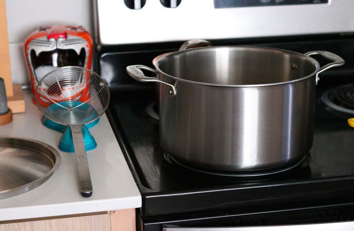 a stock pot on a stove burner and beside it is a spider strainer