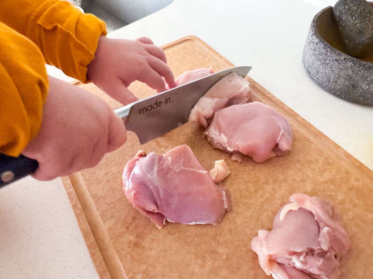 Kat is cutting the chicken thighs with a chef knife