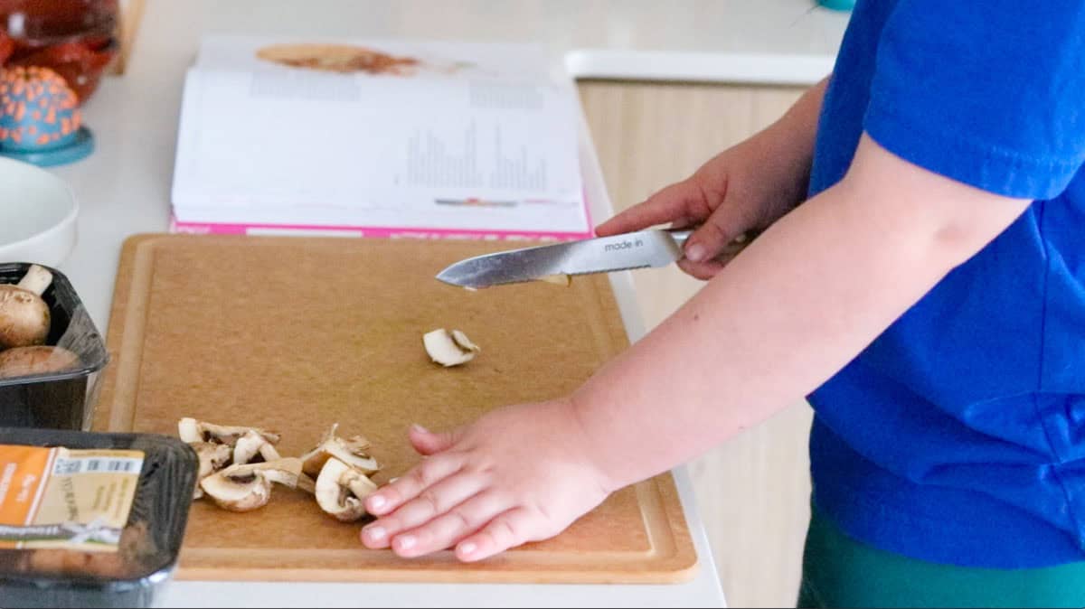 Kat is cutting mushrooms with a utility knife on a cutting board