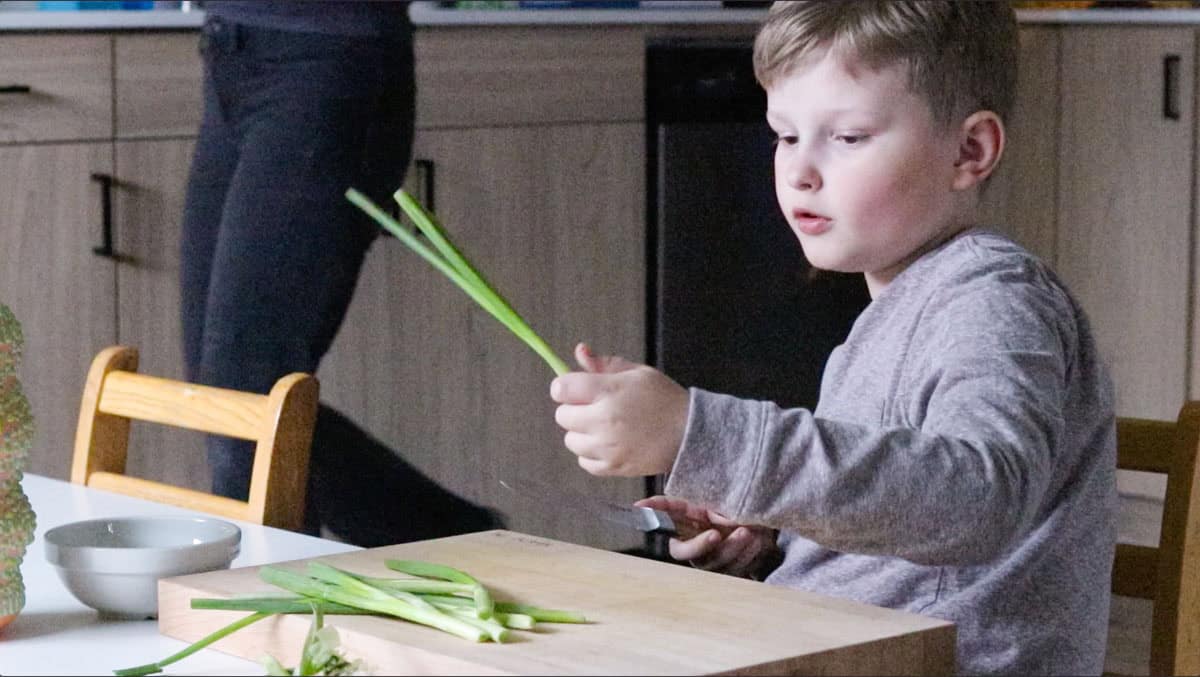 Noah is picking up scallions and holding a knife