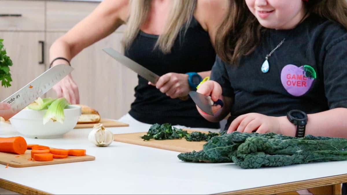 Noah, Kristin, & Kaia prepping ingredients at a table with knives and cutting boards