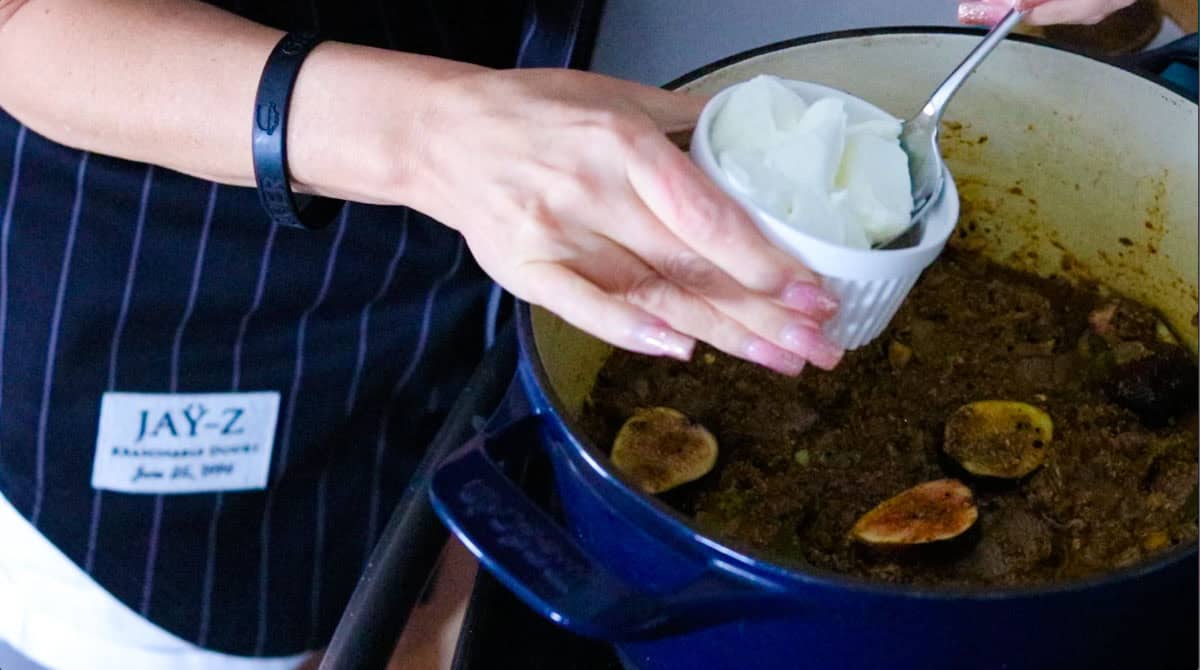 adding yogurt to a Dutch oven with biryani ingredients