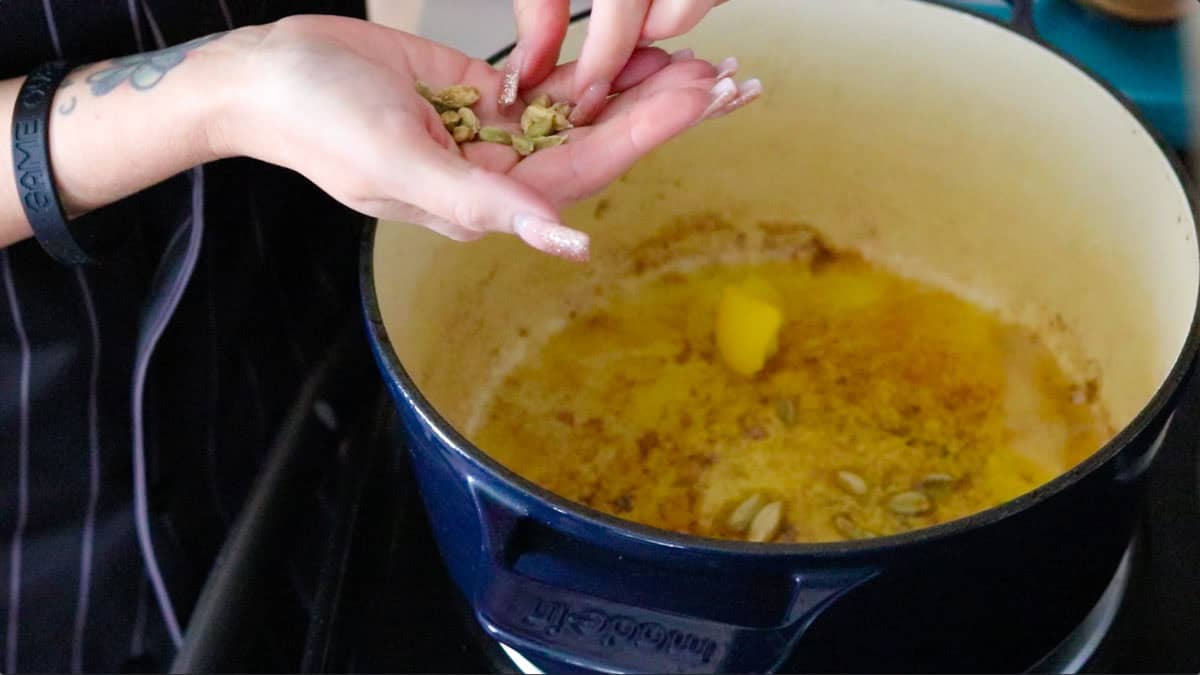 adding green cardamom pods to a Dutch oven with melted ghee