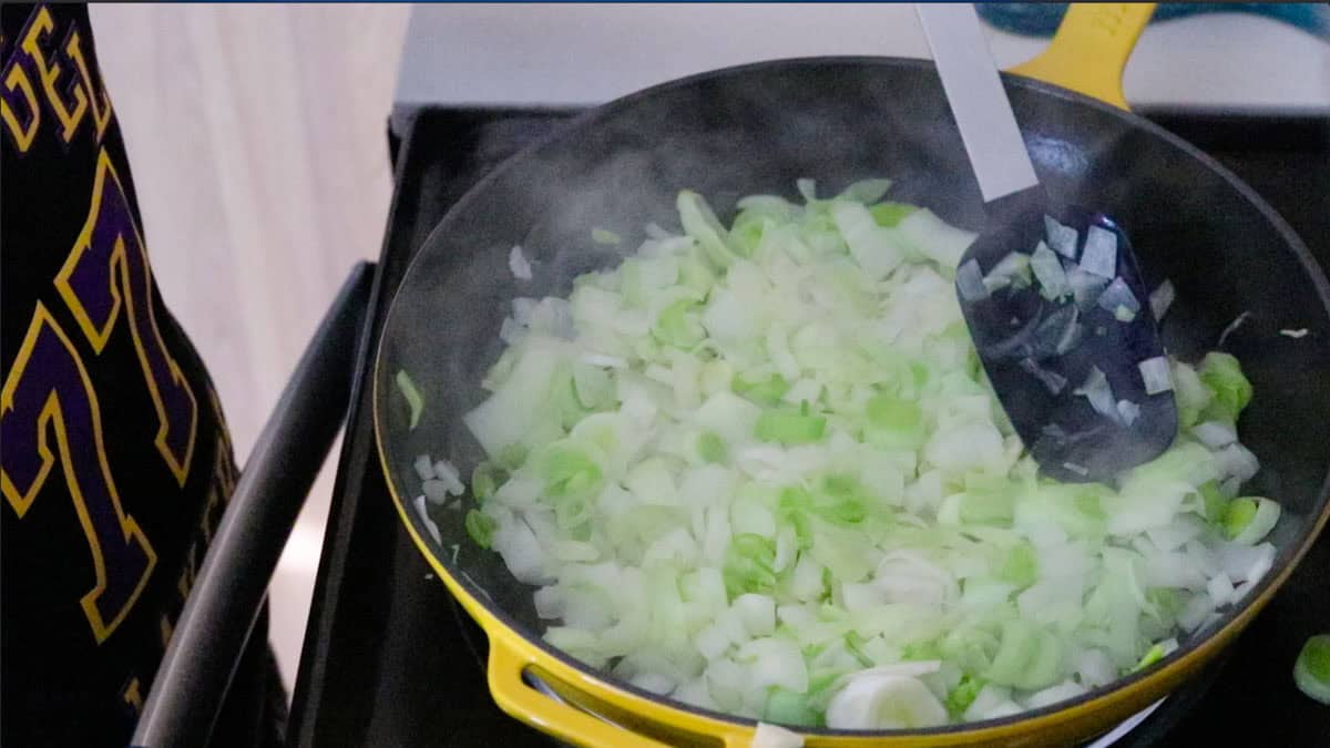 Kaia is cooking leeks and onion in a enameled cast iron skillet