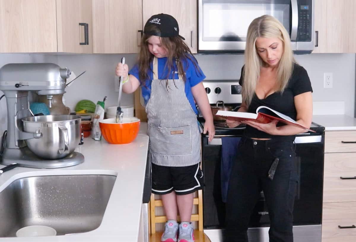 Kat is stirring the crumb cake topping ingredients and Kristin is looking at the cookbook
