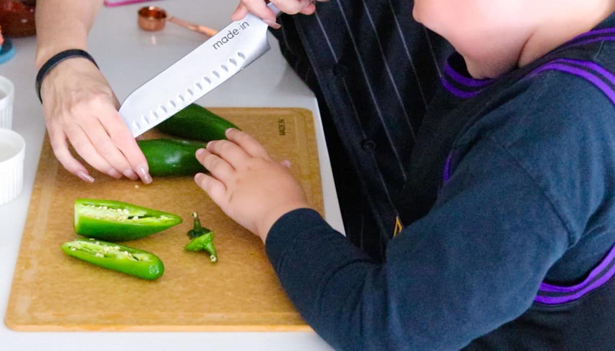Noah is using a Santoku knife with Kristin to slice down the middle of the chillies