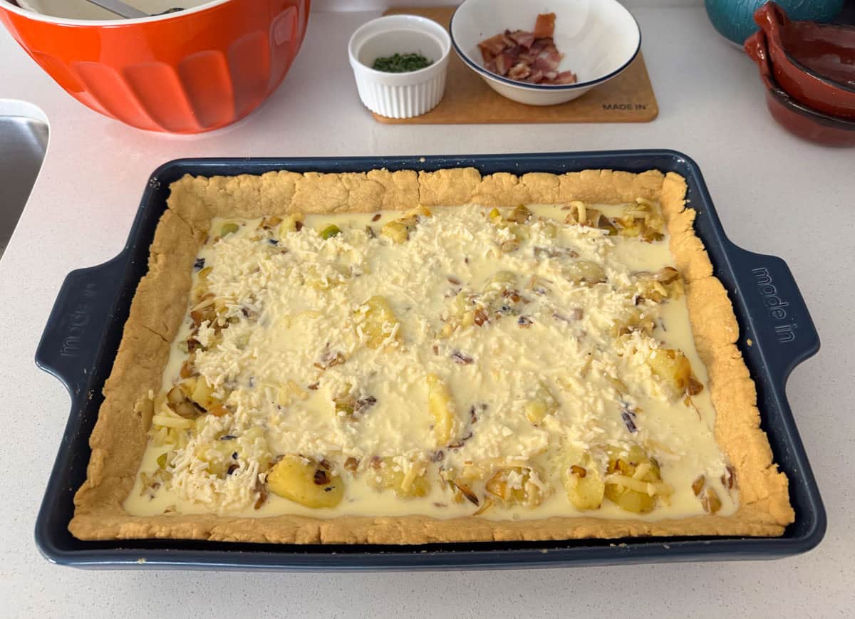 unbaked quiche lorraine with toppings behind it