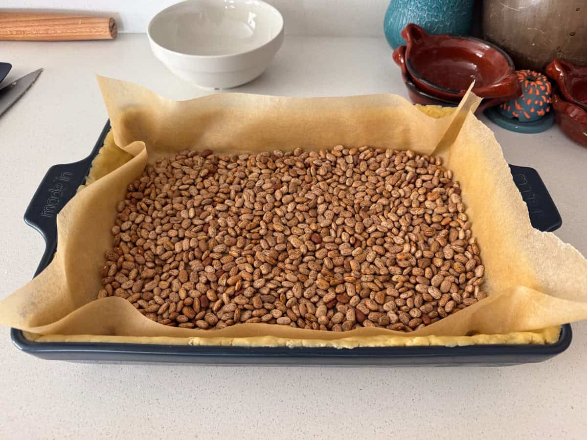 a layer of parchment paper and beans on top of quiche tart dough, ready to be baked