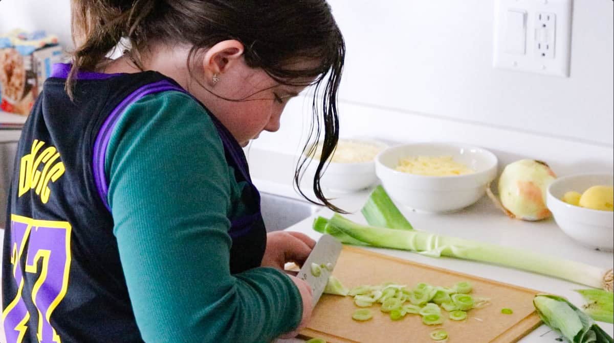 Kaia is cutting leeks at an angle with a Santoku knife