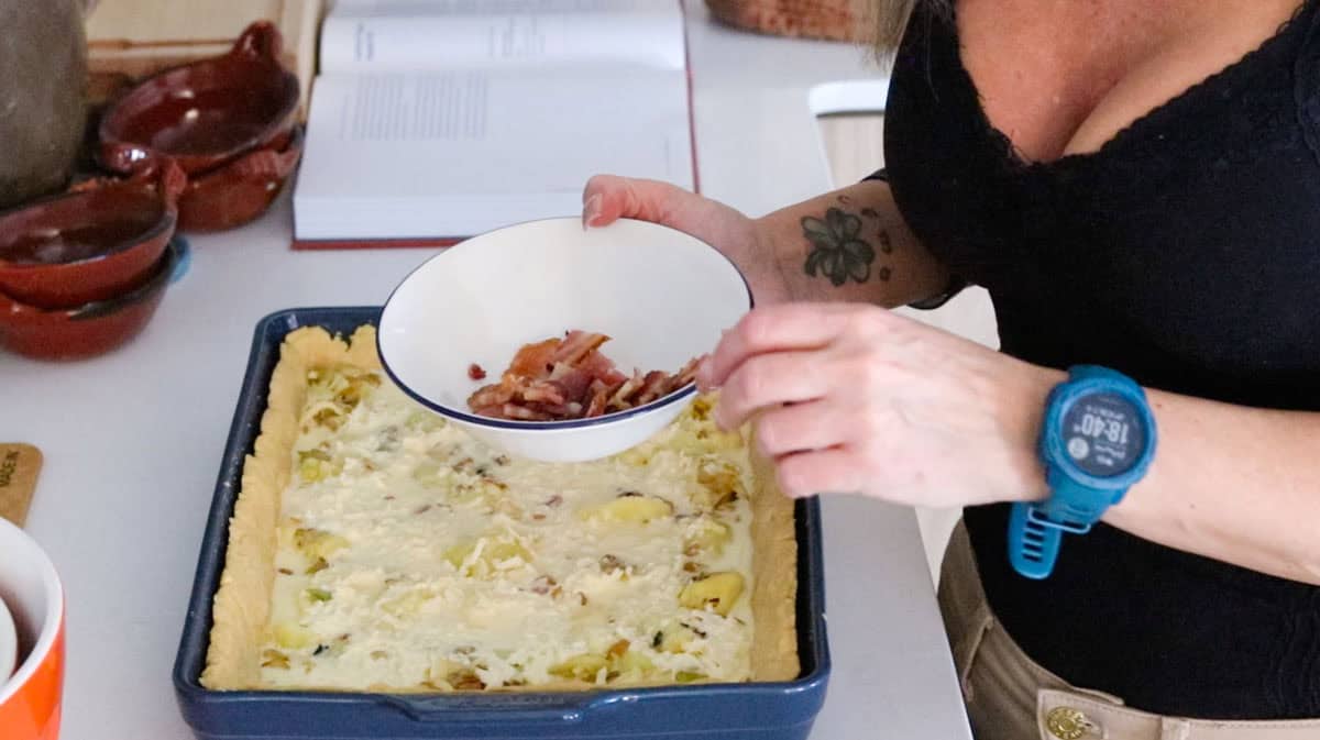 Kristin is holding cooked bacon slices over a baking dish with unbaked quiche