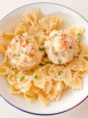 chicken piccata meatballs in a bowl with bowtie pasta and shredded parmesan