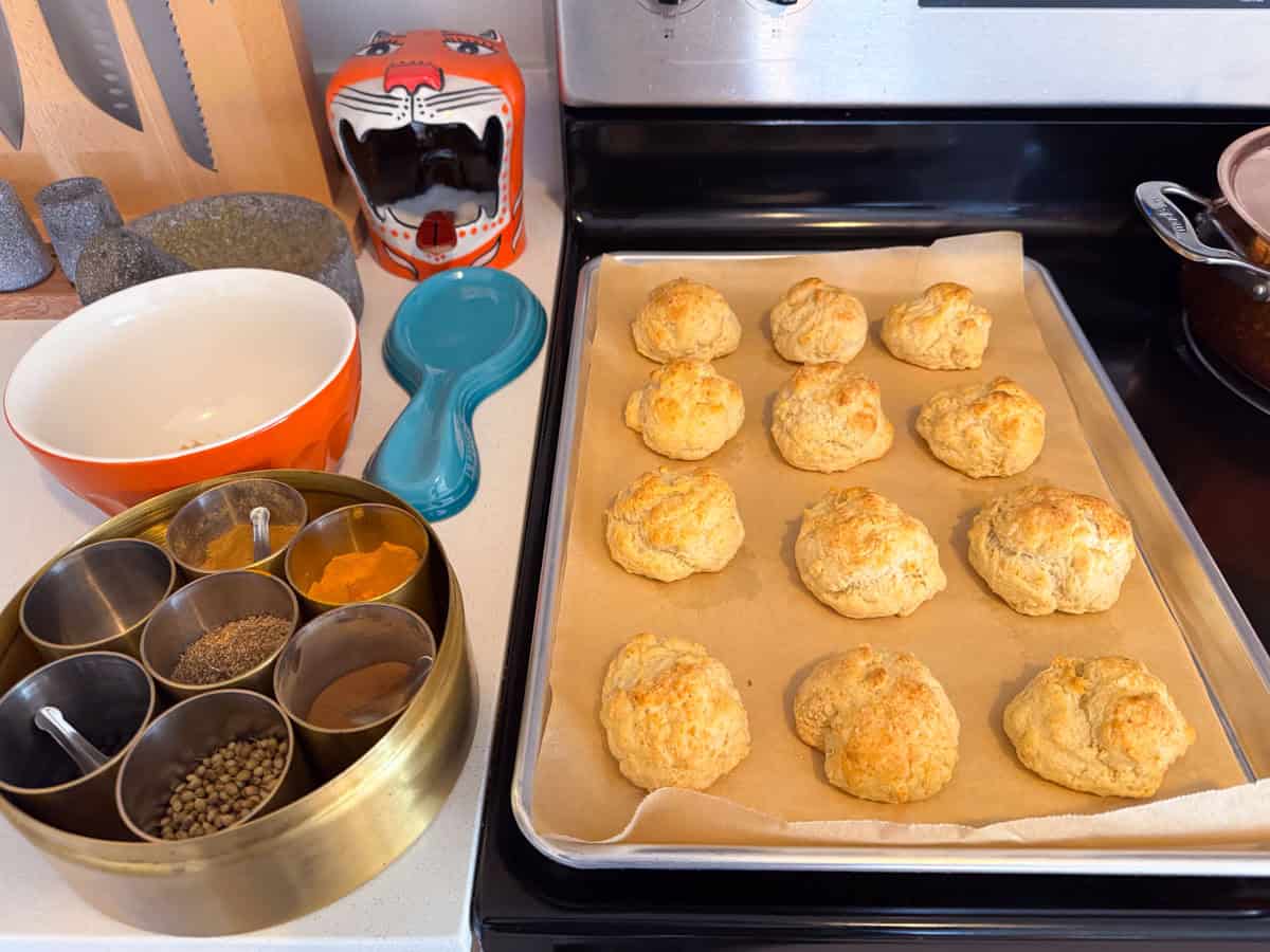 drop biscuits on a baking sheet beside a masala dabba and a bowl