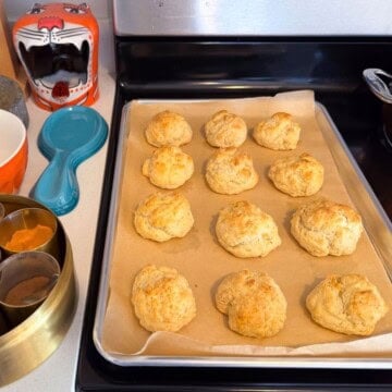 drop biscuits on a baking sheet beside a masala dabba and a bowl