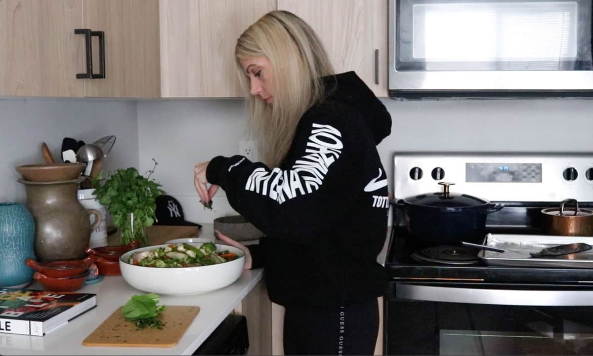 Kristin is sprinkling cilantro and mint on top of rice and roasted vegetables in a serving bowl