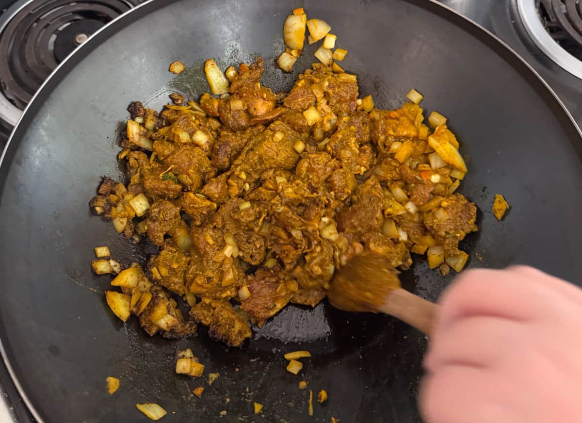 Kaia is stirring goat meat and spices in a wok