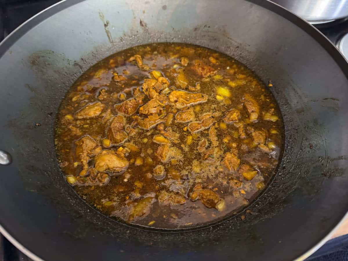 Goat meat, spices, and beef broth in a wok