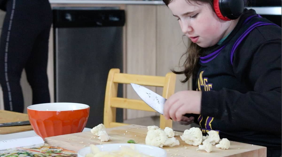 Kaia is cutting cauliflower on a butcher block