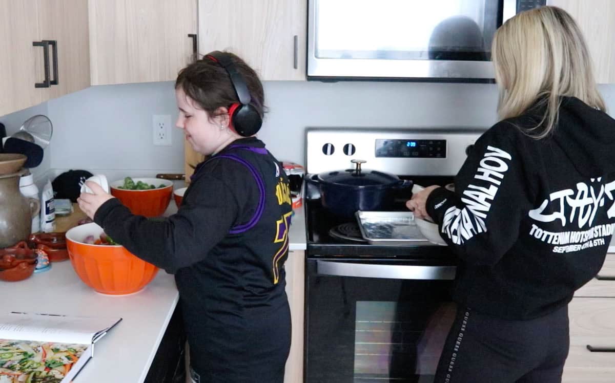 Kaia is adding spices to a bowl and Kristin is collecting used prep bowls